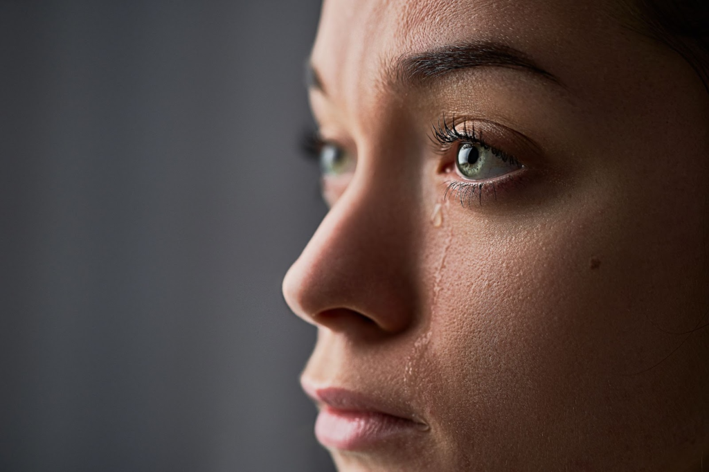 Close-up of a woman’s face with watery eyes and a tear rolling down her cheek.