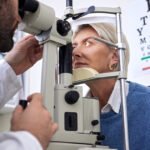 A woman is engaged in an eye exam, looking closely at the eye chart for testing her vision.